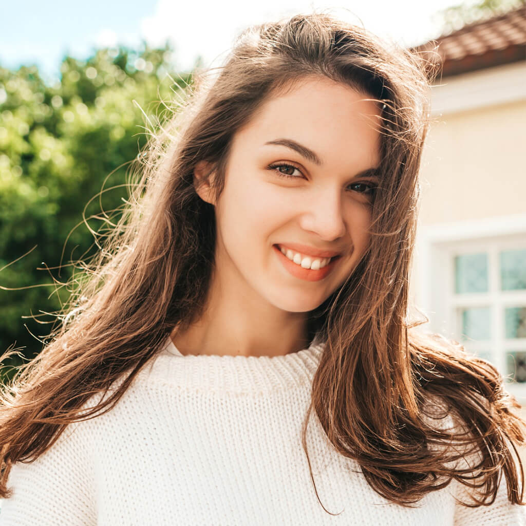 Smiling woman with long hair wearing a white sweater, showcasing radiant skin after using Luxury Honey Lifting Cream.