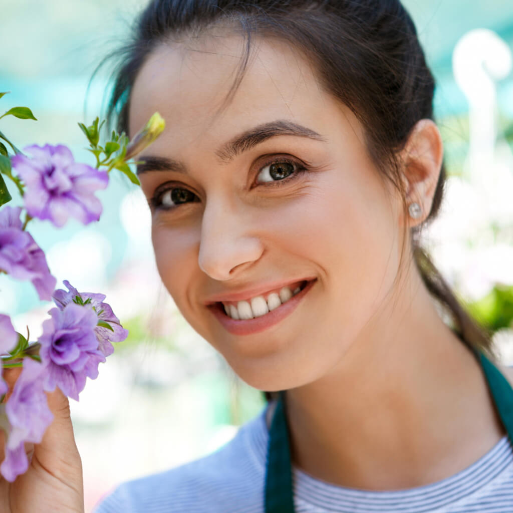 Woman smiling while holding purple flowers in a vibrant garden setting, embodying beauty and freshness.